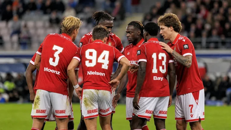 Een groep spelers van Standard Luik in rode shirts overlegt op het veld.
