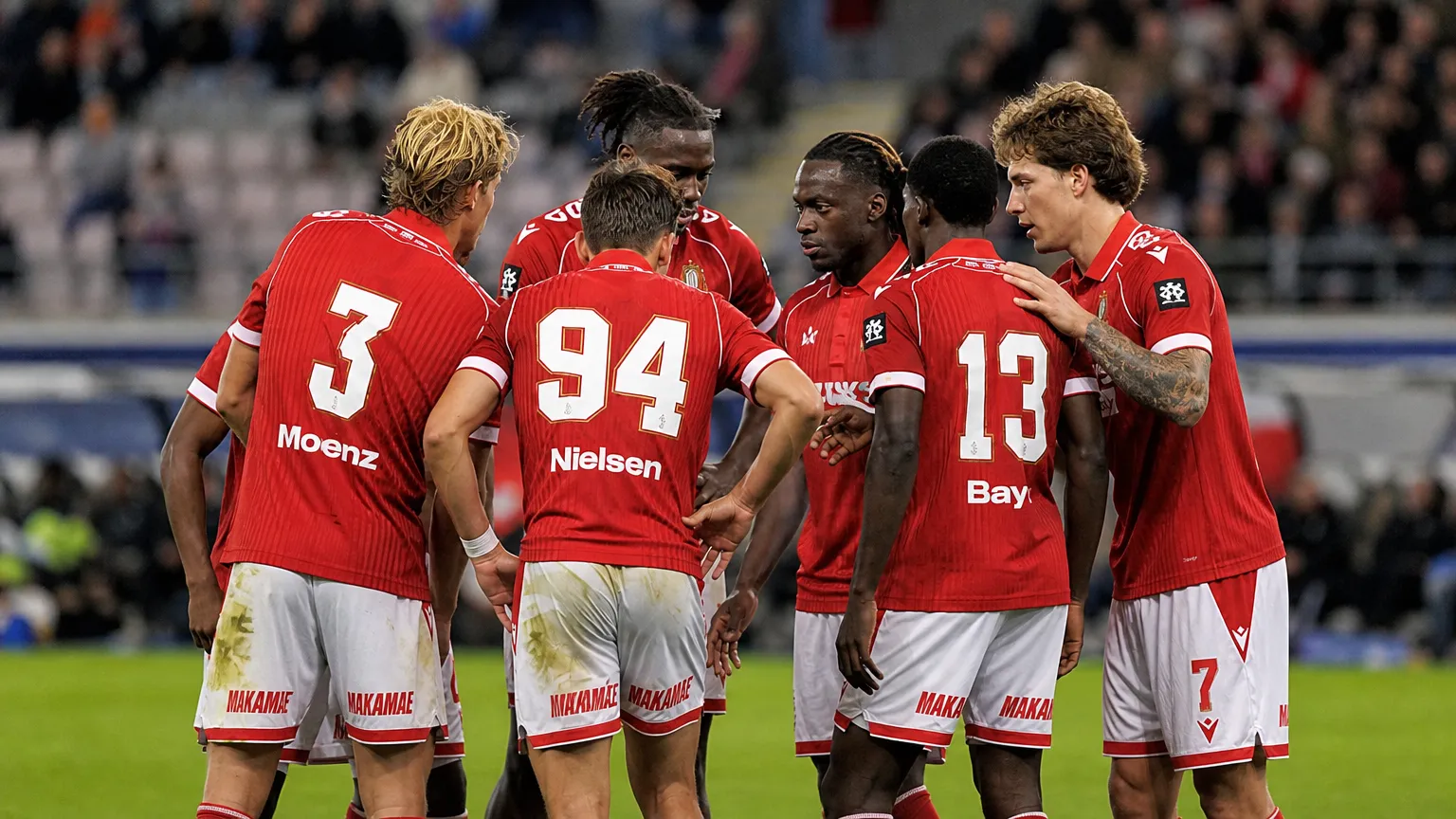 Een groep spelers van Standard Luik in rode shirts overlegt op het veld.
