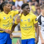Twee spelers van SK Beveren in gele shirts en blauwe broeken vieren samen een actie op het veld.
