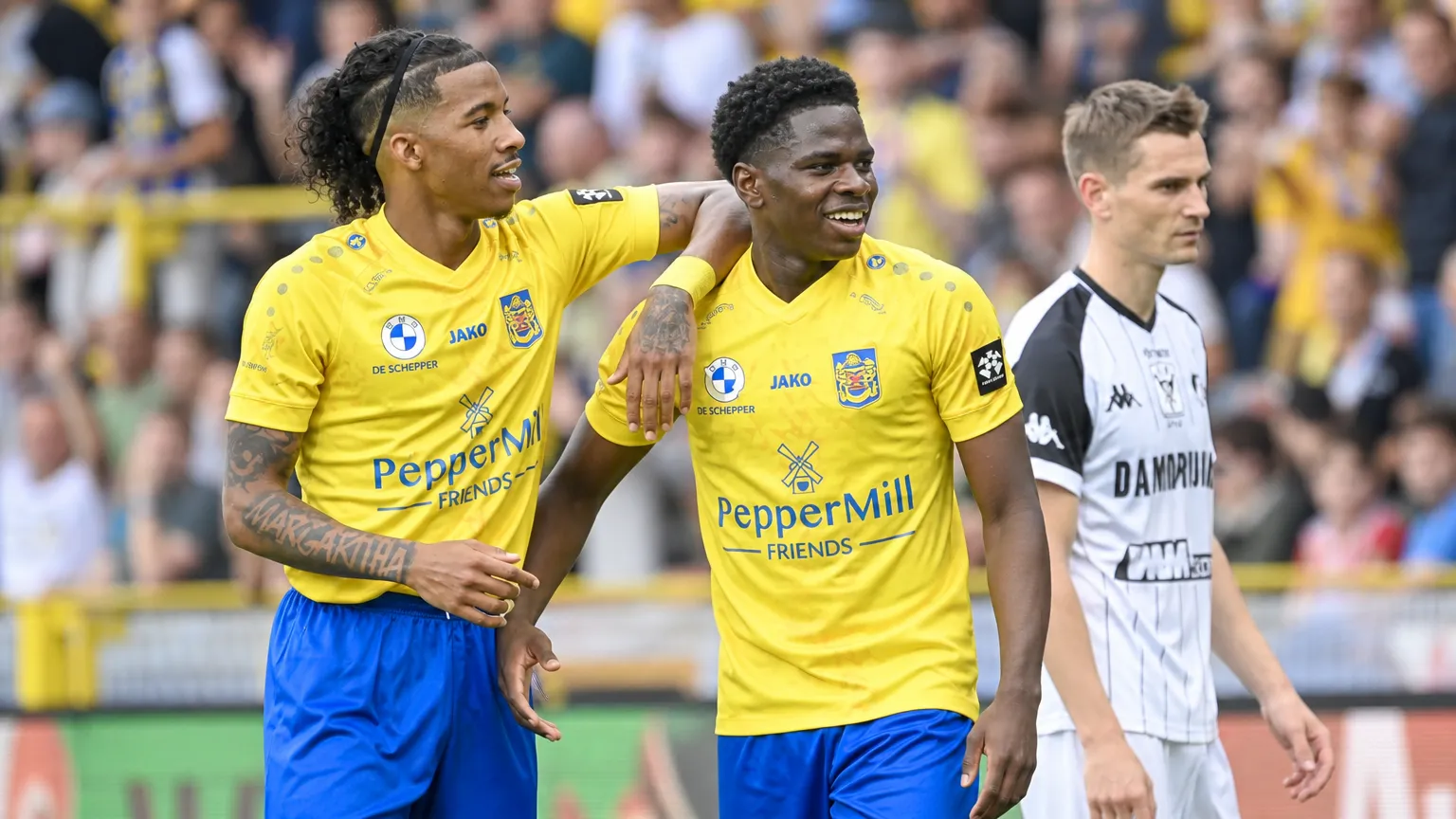 Twee spelers van SK Beveren in gele shirts en blauwe broeken vieren samen een actie op het veld.