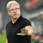 Lars Friis geeft aanwijzingen langs de zijlijn in een zwart poloshirt.