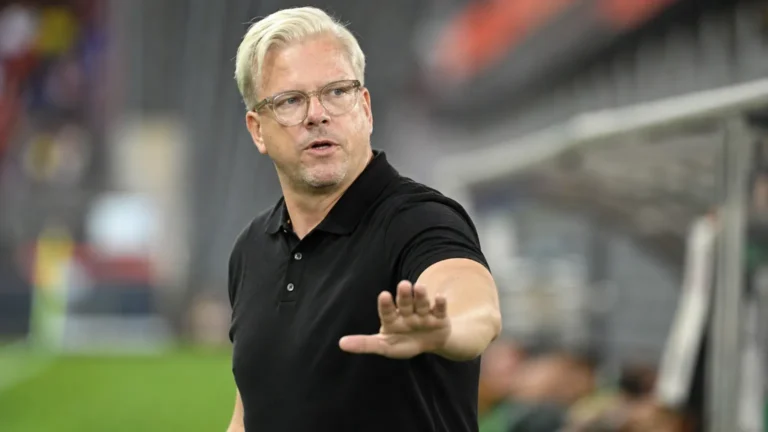 Lars Friis geeft aanwijzingen langs de zijlijn in een zwart poloshirt.