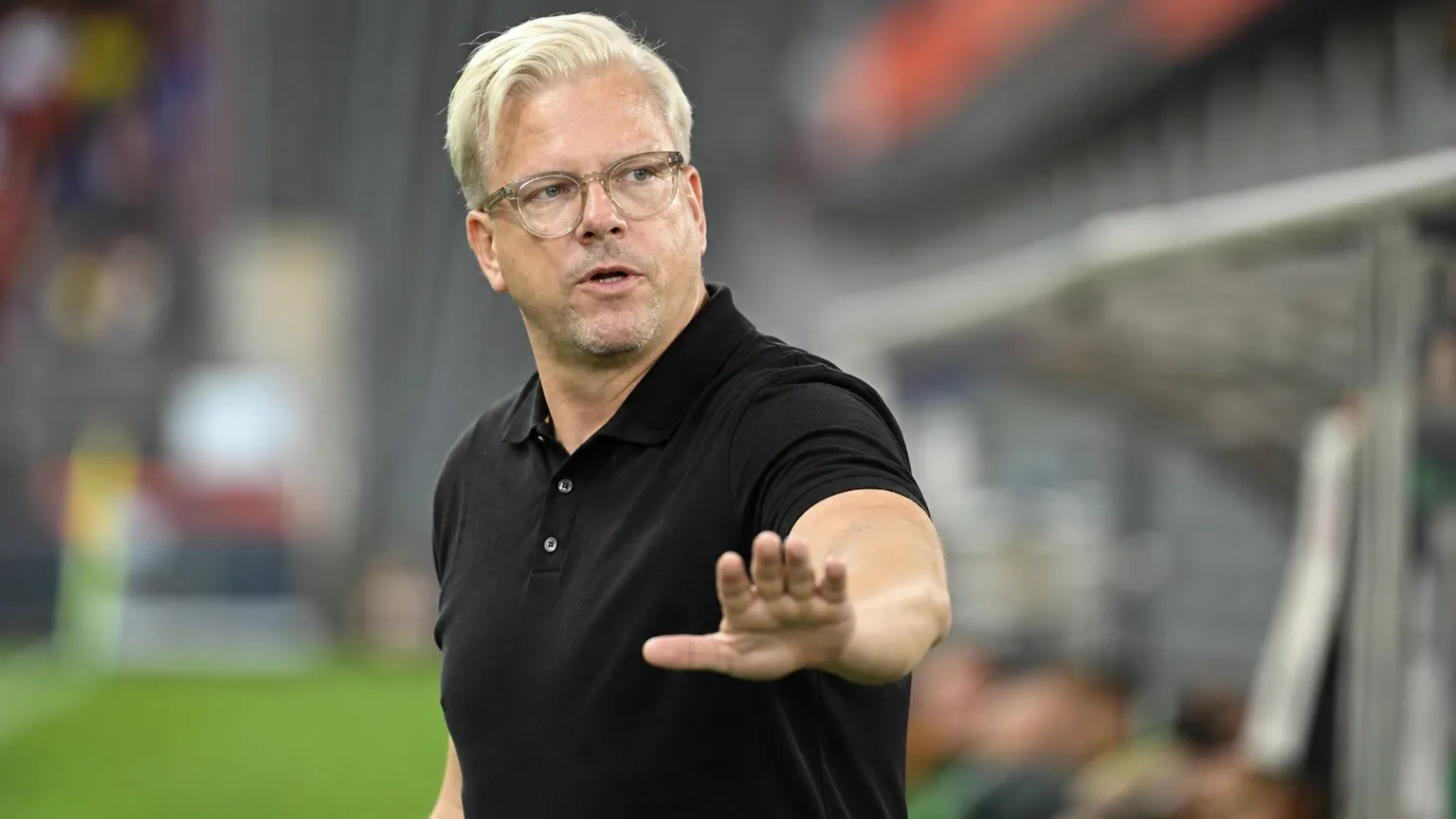 Lars Friis geeft aanwijzingen langs de zijlijn in een zwart poloshirt.