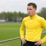 Konstantinos Karetsas in neutrale trainingskleding aan de rand van een voetbalveld.