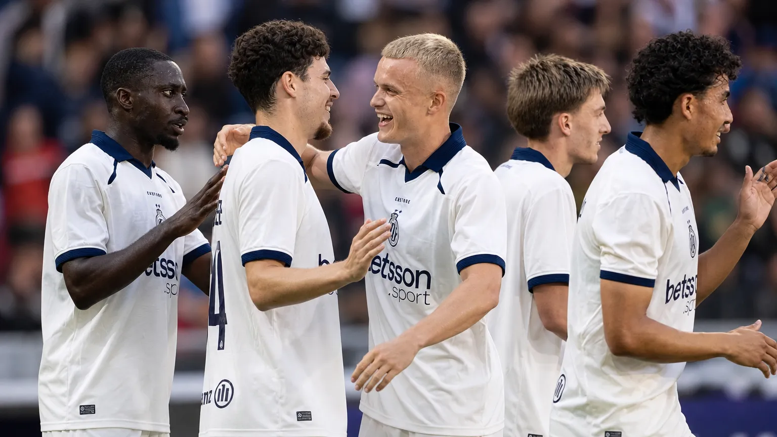 Een groep Club Brugge-spelers in witte wedstrijdshirts viert samen tijdens een wedstrijd.