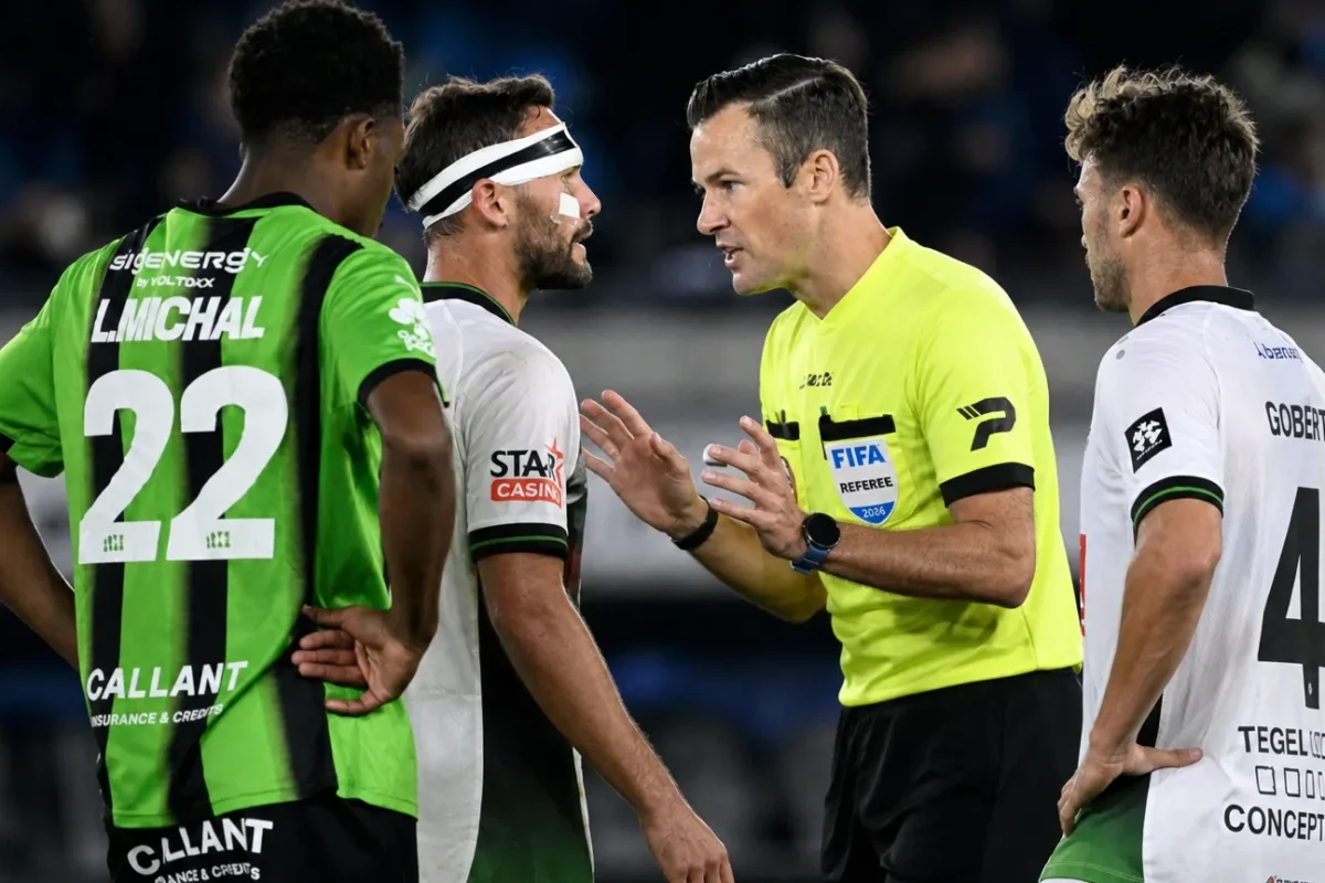 Een scheidsrechter bespreekt een fase met spelers in groene en witte wedstrijdtenues.