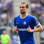 Een speler in een blauw tenue staat geconcentreerd op een voetbalveld.