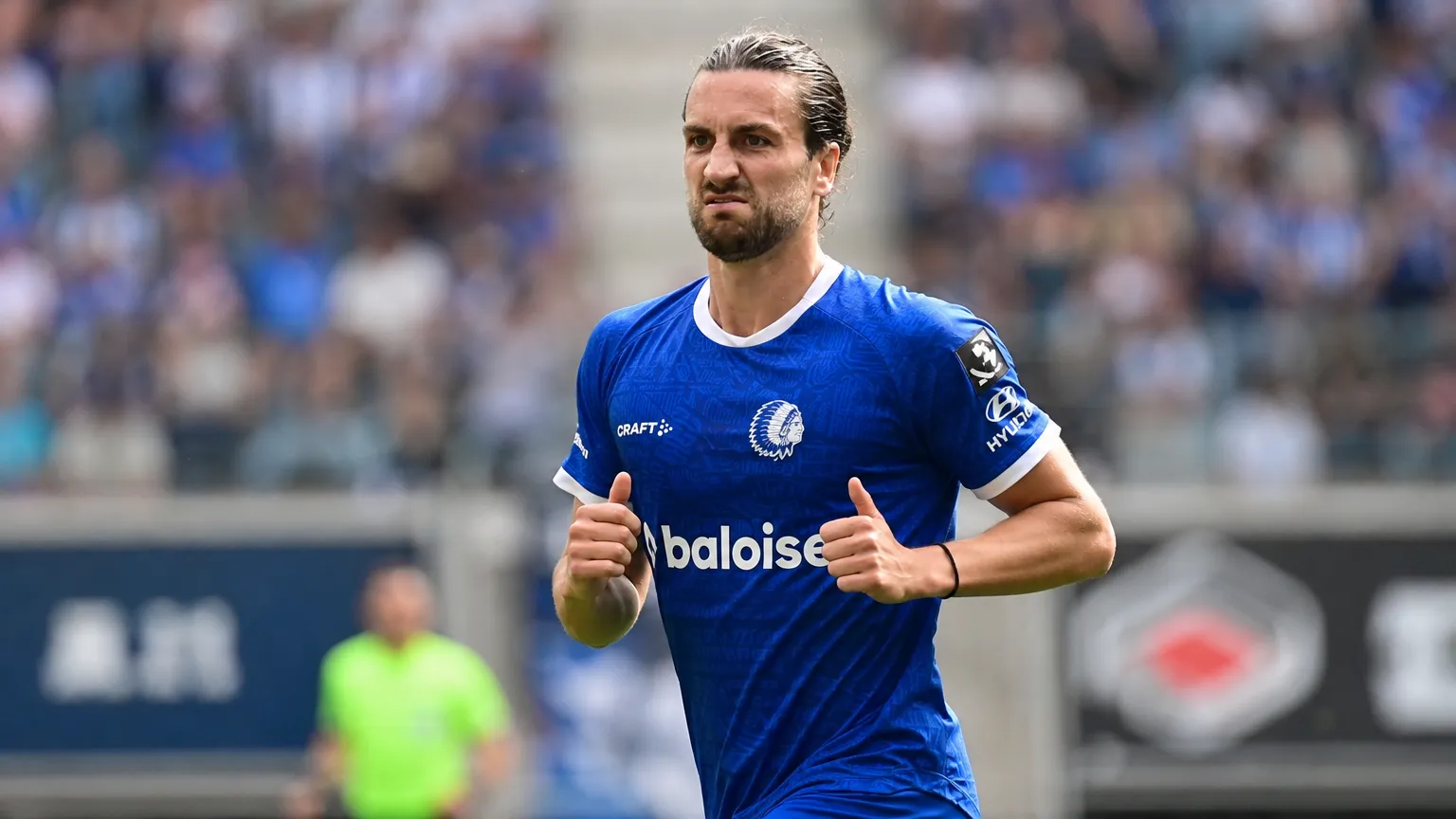 Een speler in een blauw tenue staat geconcentreerd op een voetbalveld.