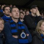 Een collectieve groep Club Brugge-supporters met blauw-zwarte sjaals in de tribune.