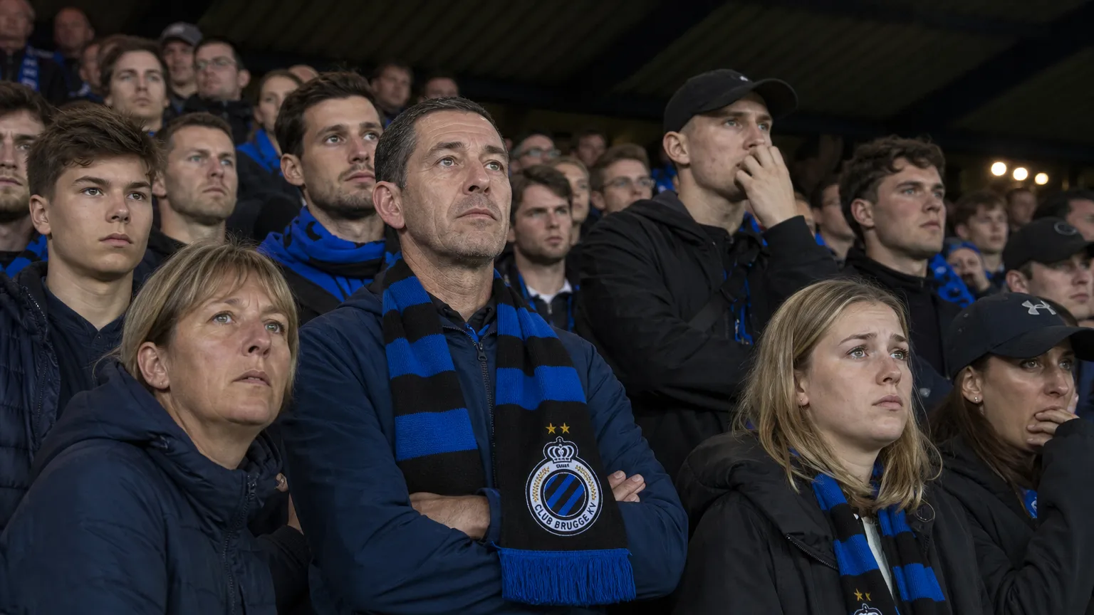 Een collectieve groep Club Brugge-supporters met blauw-zwarte sjaals in de tribune.