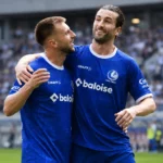 Twee KAA Gent-spelers vieren samen een moment op het veld.