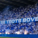 Collectieve KRC Genk-supporters met blauw-witte vlaggen op de thuistribune voor de aftrap.