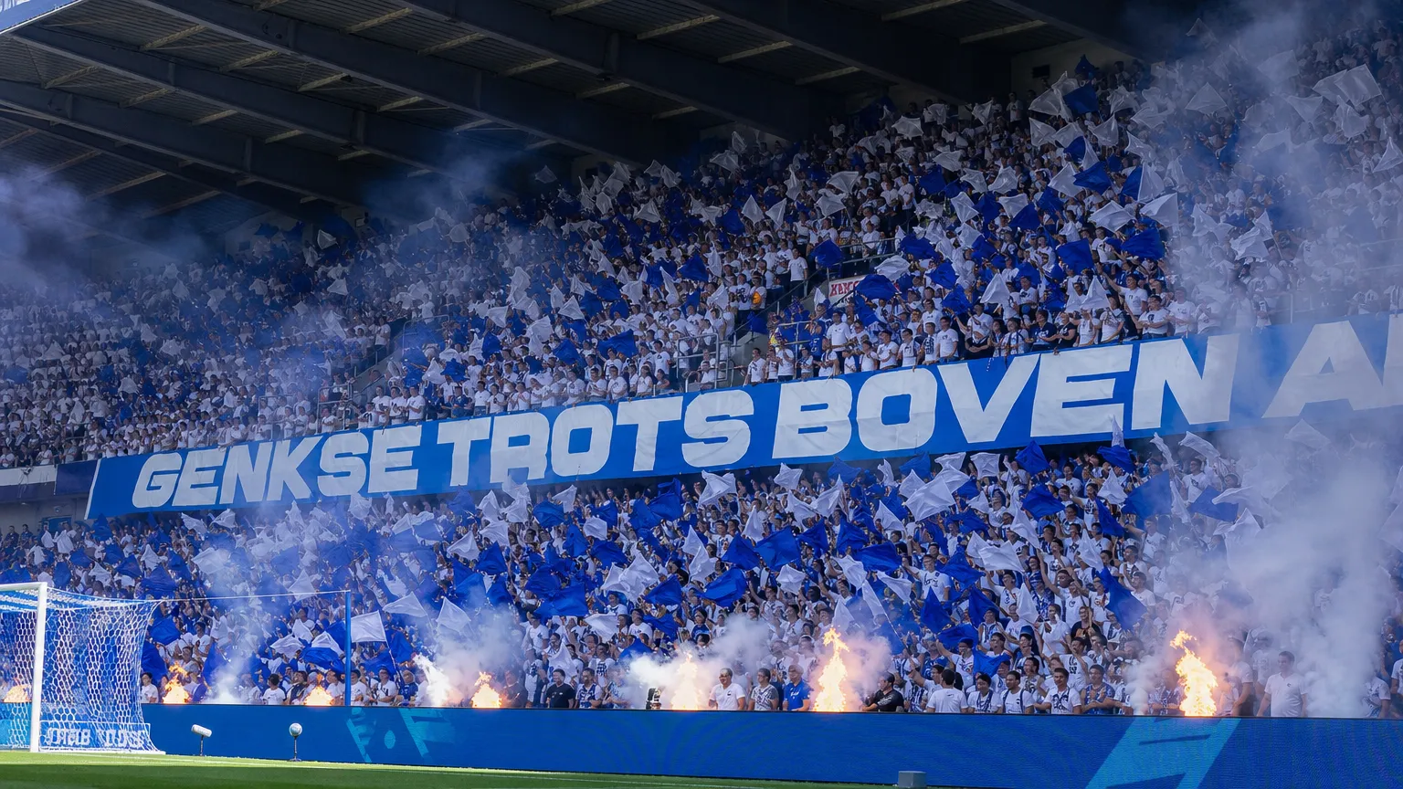 Collectieve KRC Genk-supporters met blauw-witte vlaggen op de thuistribune voor de aftrap.