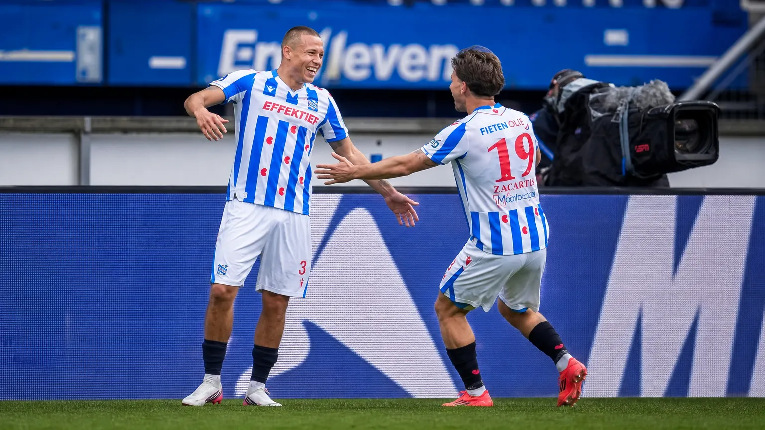 Twee spelers van sc Heerenveen vieren samen een moment langs het veld.