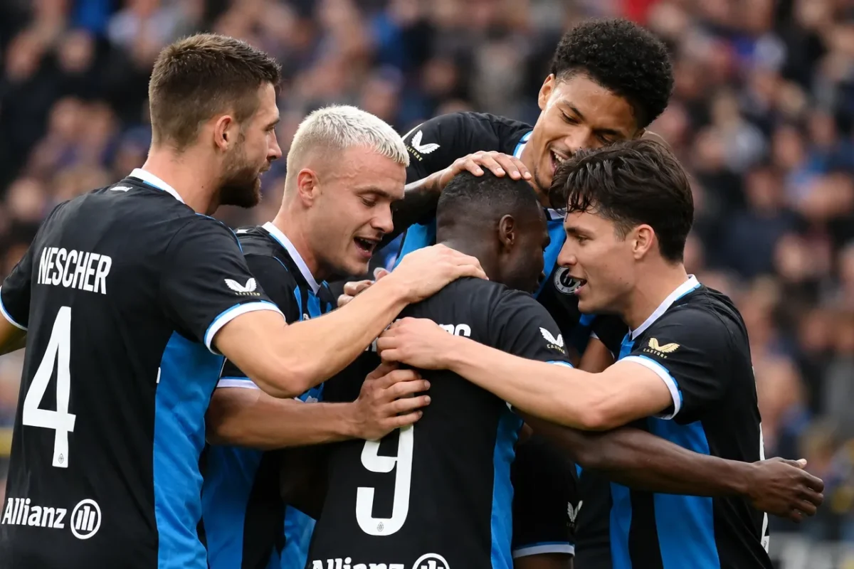 Club Brugge-spelers in zwart-blauwe tenues vormen een hechte kring op het veld.