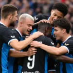 Club Brugge-spelers in zwart-blauwe tenues vormen een hechte kring op het veld.