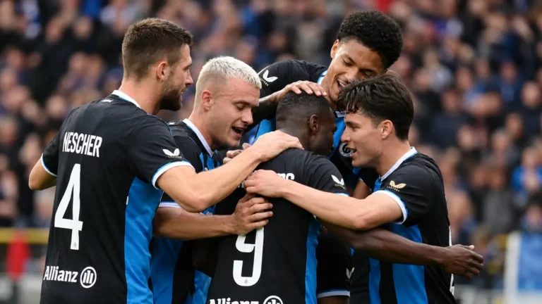 Club Brugge-spelers in zwart-blauwe tenues vormen een hechte kring op het veld.