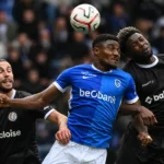 Spelers van KRC Genk en KAA Gent in een luchtduel tijdens de wedstrijd.