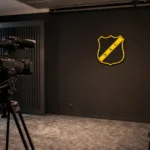 Voorbereide clubmediastudio van NAC Breda met camera-apparatuur en een NAC-embleem aan de wand.