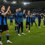 Een groep voetballers in blauw-zwarte tenues applaudisseert op het veld voor de thuistribune.