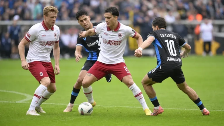 Voetballers in witte en donkere tenues tijdens een duel op het veld.