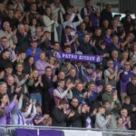 Supporters van Patro Eisden applaudisseren op de thuistribune met een clubsjaal.