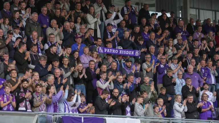 Supporters van Patro Eisden applaudisseren op de thuistribune met een clubsjaal.