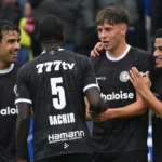 Een groep KAA Gent-spelers in zwarte wedstrijdshirts verzamelt zich na de wedstrijd aan de rand van het veld.