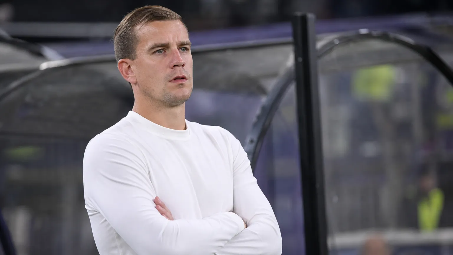 Michiel Jonckheere staat in een witte trui langs de zijlijn van een voetbalstadion.