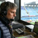 Een voetbalcommentator met headset in een radiocabine van een stadion.