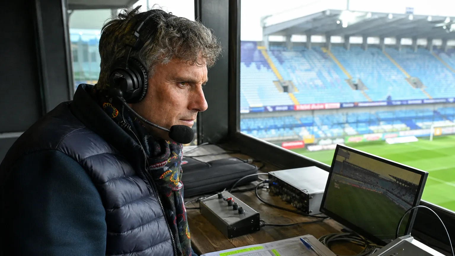 Een voetbalcommentator met headset in een radiocabine van een stadion.