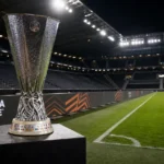 De Europa League-trofee op een podium langs een verlicht stadionveld.