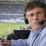 Peter Vandenbempt met headset in een commentaarcabine tijdens een voetbalwedstrijd.