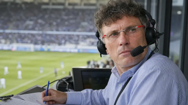 Peter Vandenbempt met headset in een commentaarcabine tijdens een voetbalwedstrijd.