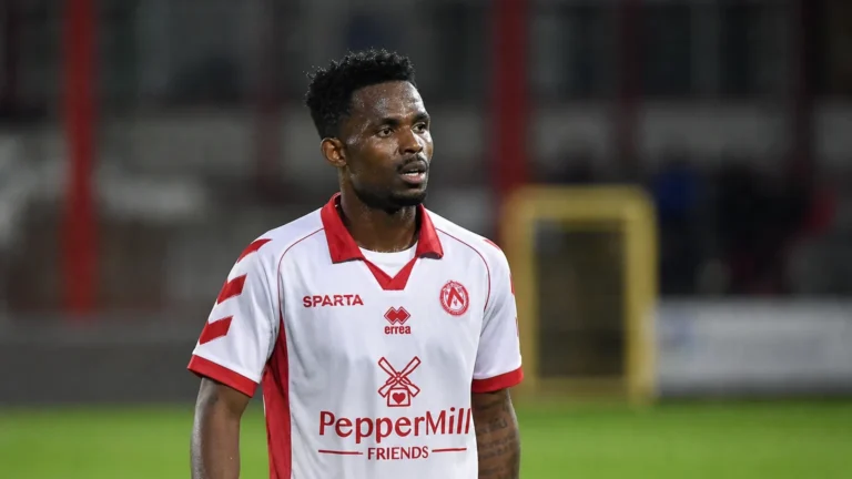 Een voetballer in een wit-rood tenue reageert ontgoocheld op het veld na een wedstrijd.