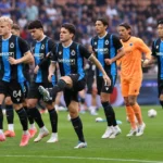 Een groep spelers in zwart-blauwe tenues warmt op het veld op.