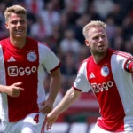 Twee Ajax-spelers in rood-witte tenues tijdens een nieuw wedstrijdmoment op het veld.