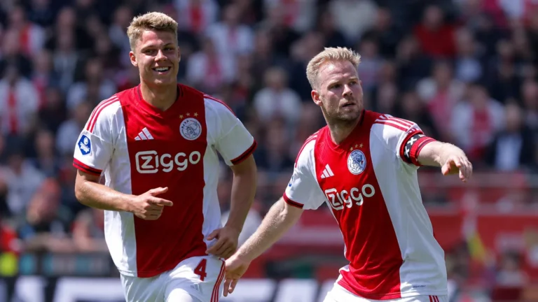 Twee Ajax-spelers in rood-witte tenues tijdens een nieuw wedstrijdmoment op het veld.