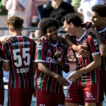 Een groep voetballers in rood-groen-wit gestreepte shirts viert samen naast de tribune.