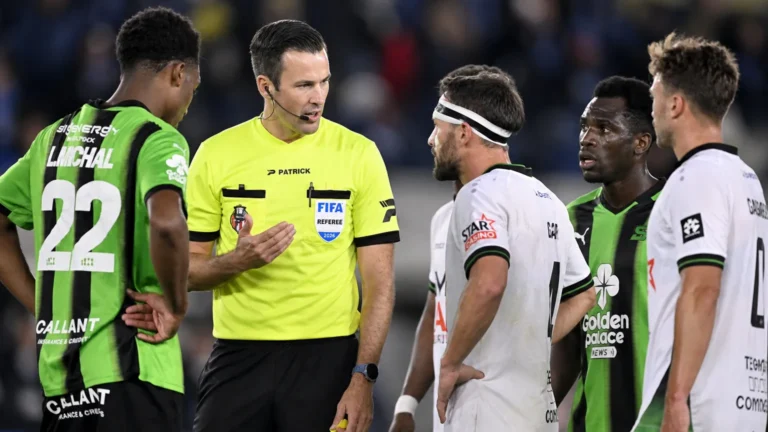 Een scheidsrechter spreekt op het veld met spelers tijdens een Belgische competitiewedstrijd.
