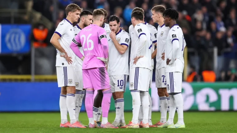 Een groep Anderlecht-spelers overlegt in een kring op het veld, met een doelman in roze tenue.