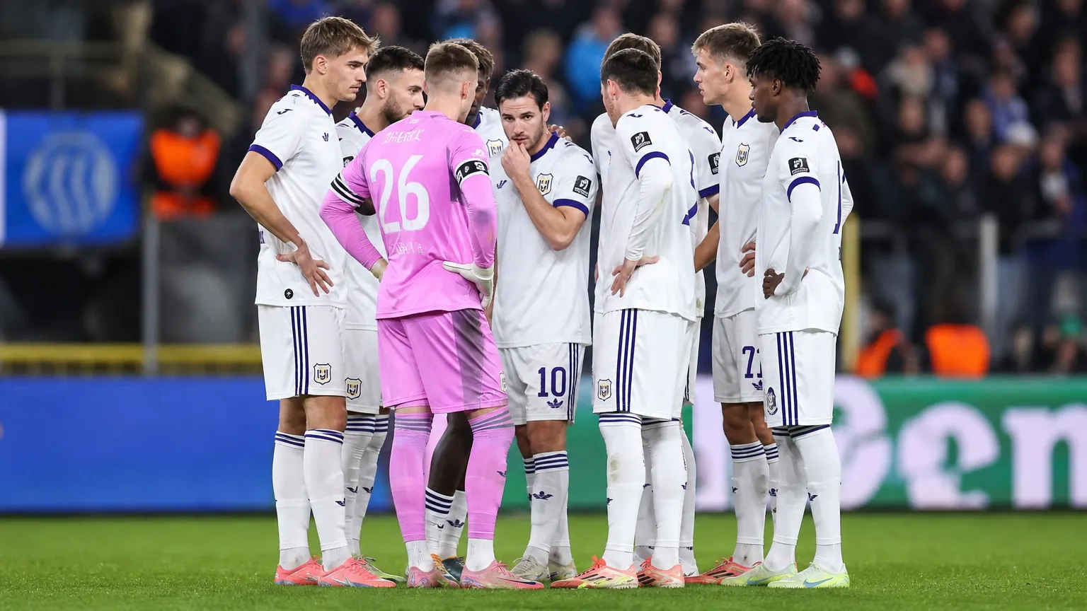 Een groep Anderlecht-spelers overlegt in een kring op het veld, met een doelman in roze tenue.