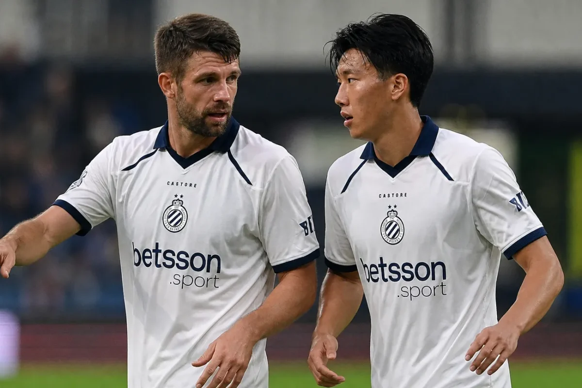 Twee Club Brugge-spelers in witte tenues overleggen tijdens een wedstrijdmoment.