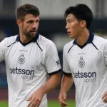 Twee Club Brugge-spelers in witte tenues overleggen tijdens een wedstrijdmoment.