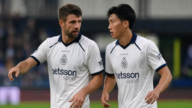 Twee Club Brugge-spelers in witte tenues overleggen tijdens een wedstrijdmoment.