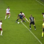 Spelers en een scheidsrechter in actie in het strafschopgebied tijdens een wedstrijd.