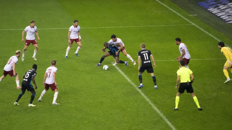 Spelers en een scheidsrechter in actie in het strafschopgebied tijdens een wedstrijd.