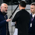 Drie clubmedewerkers in gesprek aan de rand van een stadiontribune.