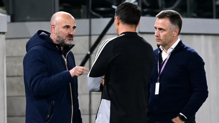 Drie clubmedewerkers in gesprek aan de rand van een stadiontribune.