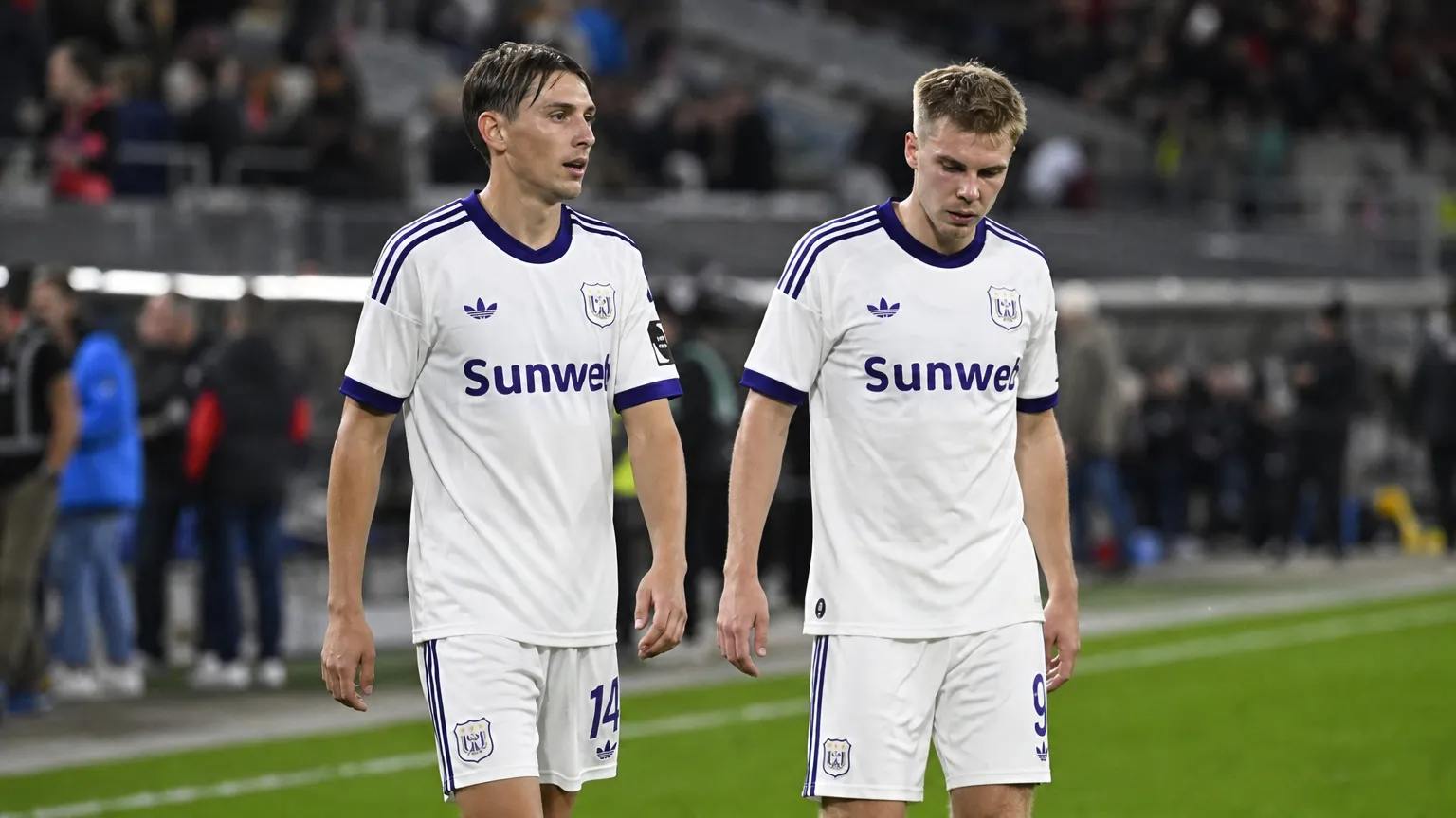 Twee Anderlecht-spelers wandelen na de wedstrijd over het veld.